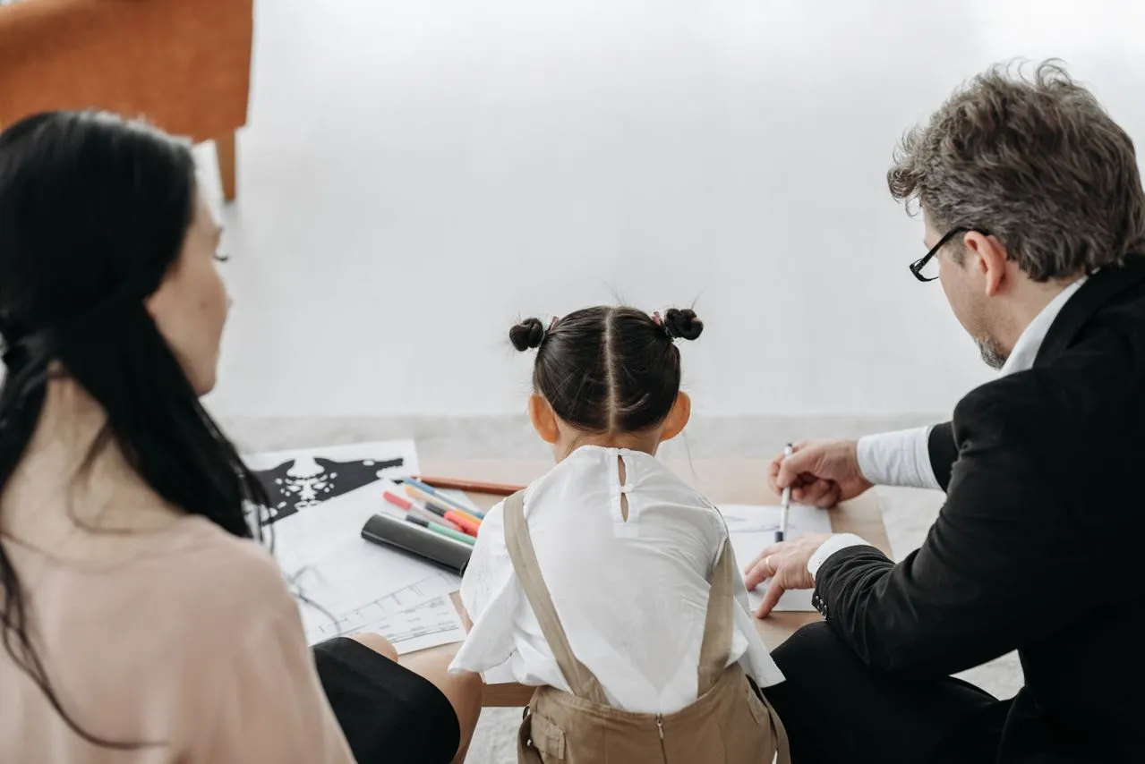 Parents sitting with young daughter drawing on paper during a focused Co-Parent Coaching session for guidance.
