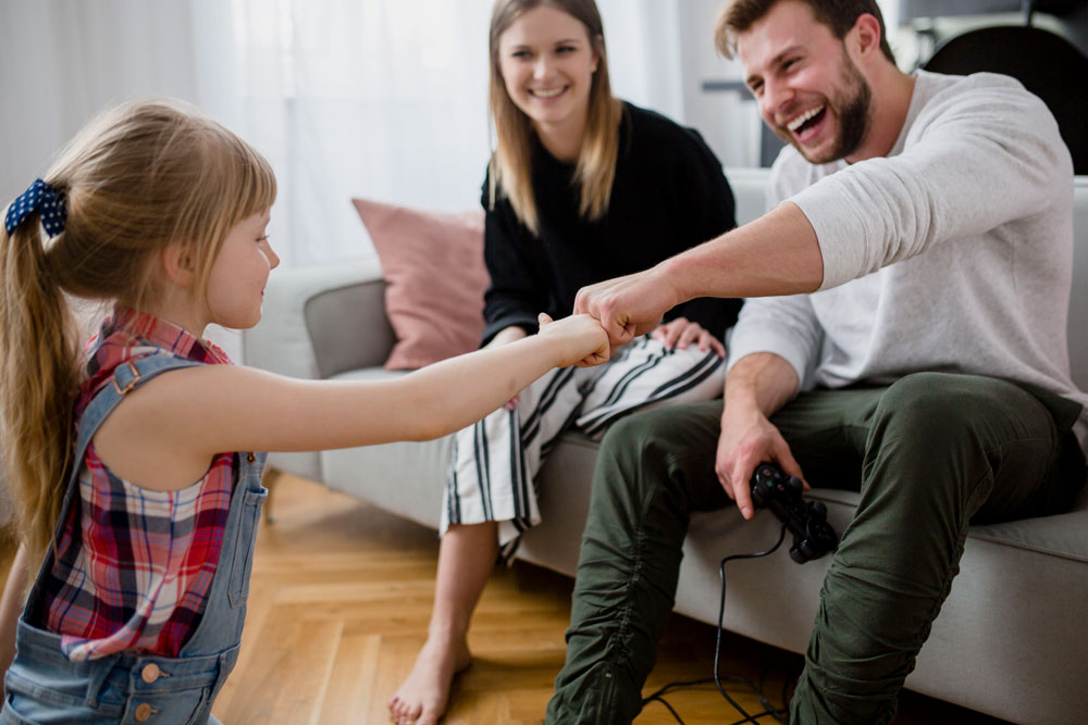 Smiling father fist bumping his young daughter while mother watches happily on the sofa during a co-parent coaching session