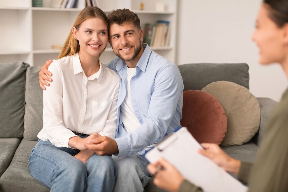 Young smiling couple holding hands on a couch while attending a therapy session to navigate family estrangement