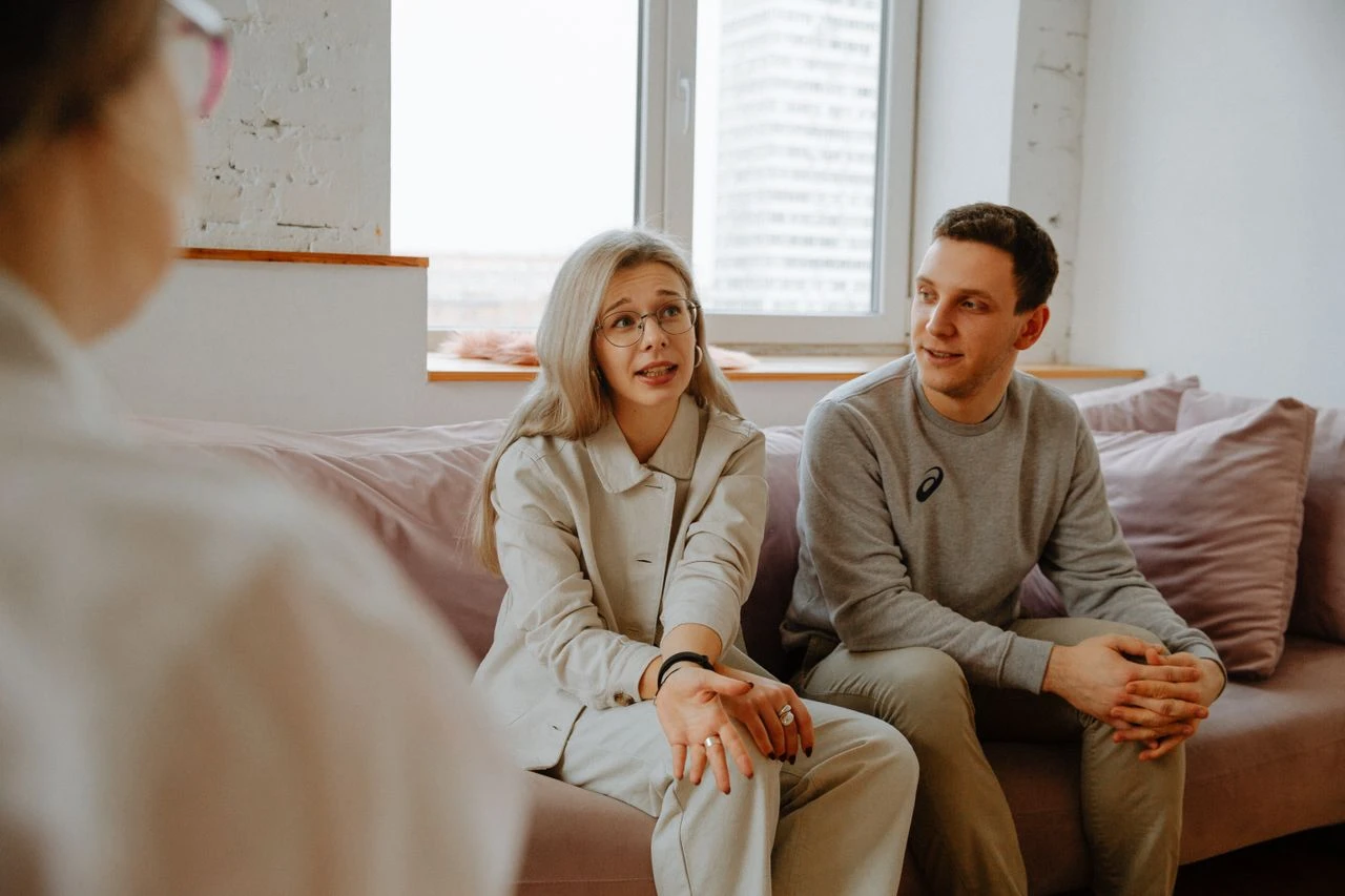 Young woman speaking and gesturing to a counselor while sitting next to her partner during a couples therapy session.