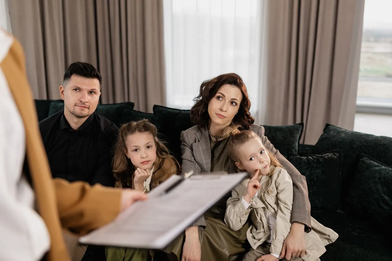 Parents and two daughters sitting on a sofa listening to a specialist during an attentive Parent Coaching session.