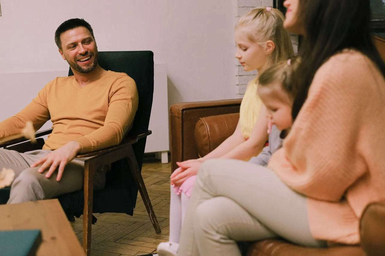 Smiling father sitting on an armchair talking with his family during a supportive Parent Coaching counseling session.