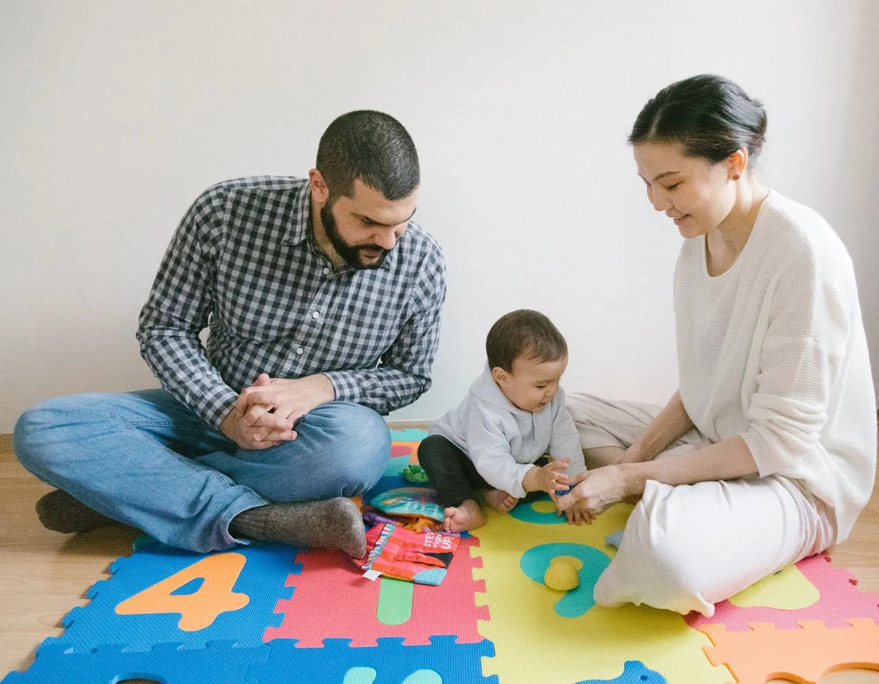 Mother and father playing on a colorful foam mat with their baby during an interactive Parent Coaching session.